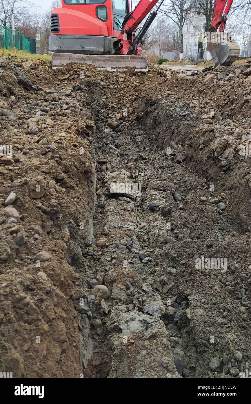 Un escavatore scava una trincea per liquame e acqua piovana lungo la strada, un escavatore cingolato. Foto Stock