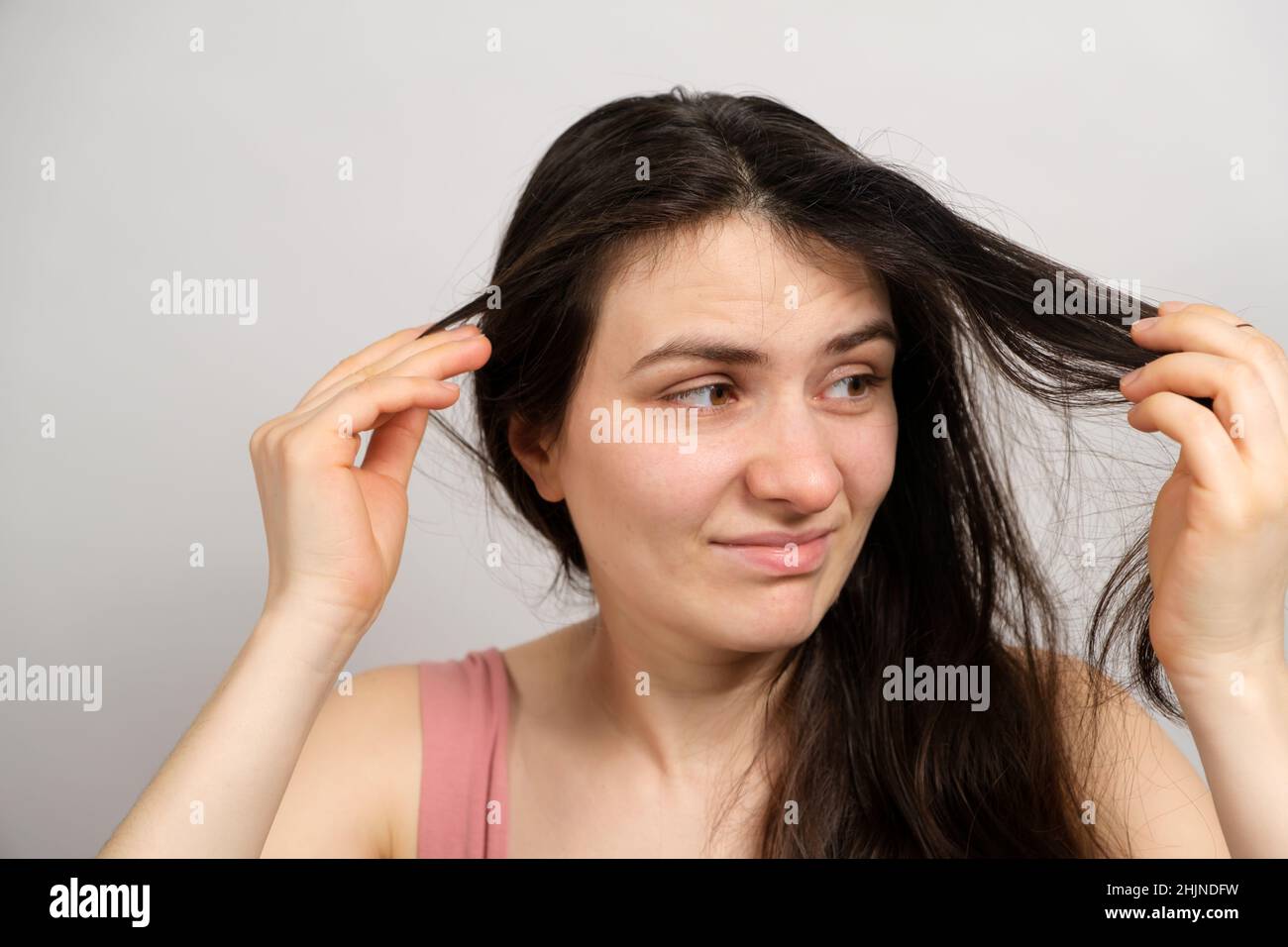 Una bella donna bruna senza trucco con capelli sporchi oleosi tiene le mani sulla testa con uno sguardo insoddisfatto Foto Stock