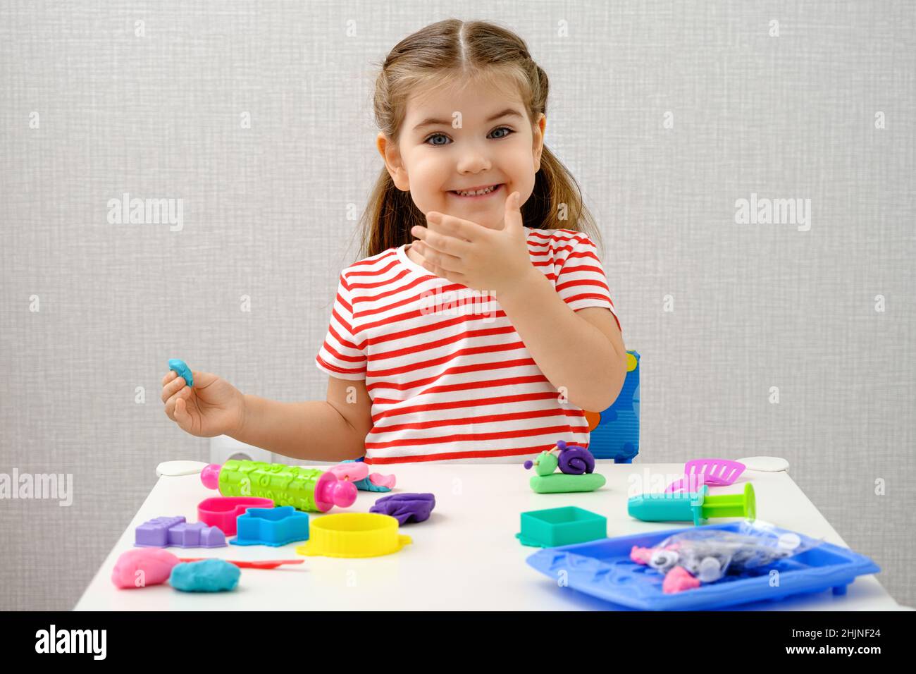 sorridente bambina che gioca con plastilina colorata, argilla, pasta da  gioco su tavola bianca, giochi educativi a casa, concetto di infanzia  felice Foto stock - Alamy