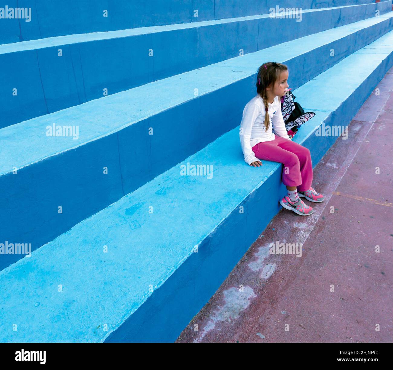 Ragazza, 5-7 anni, seduta in attesa, fissando avanti. Foto Stock