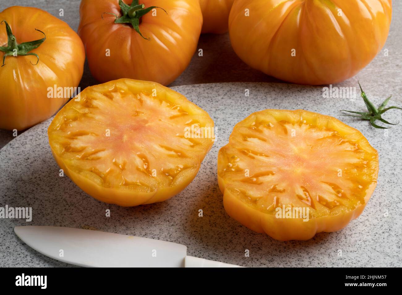 Metà succosa giallo coeur de boeuf pomodoro in primo piano e interi in background Foto Stock