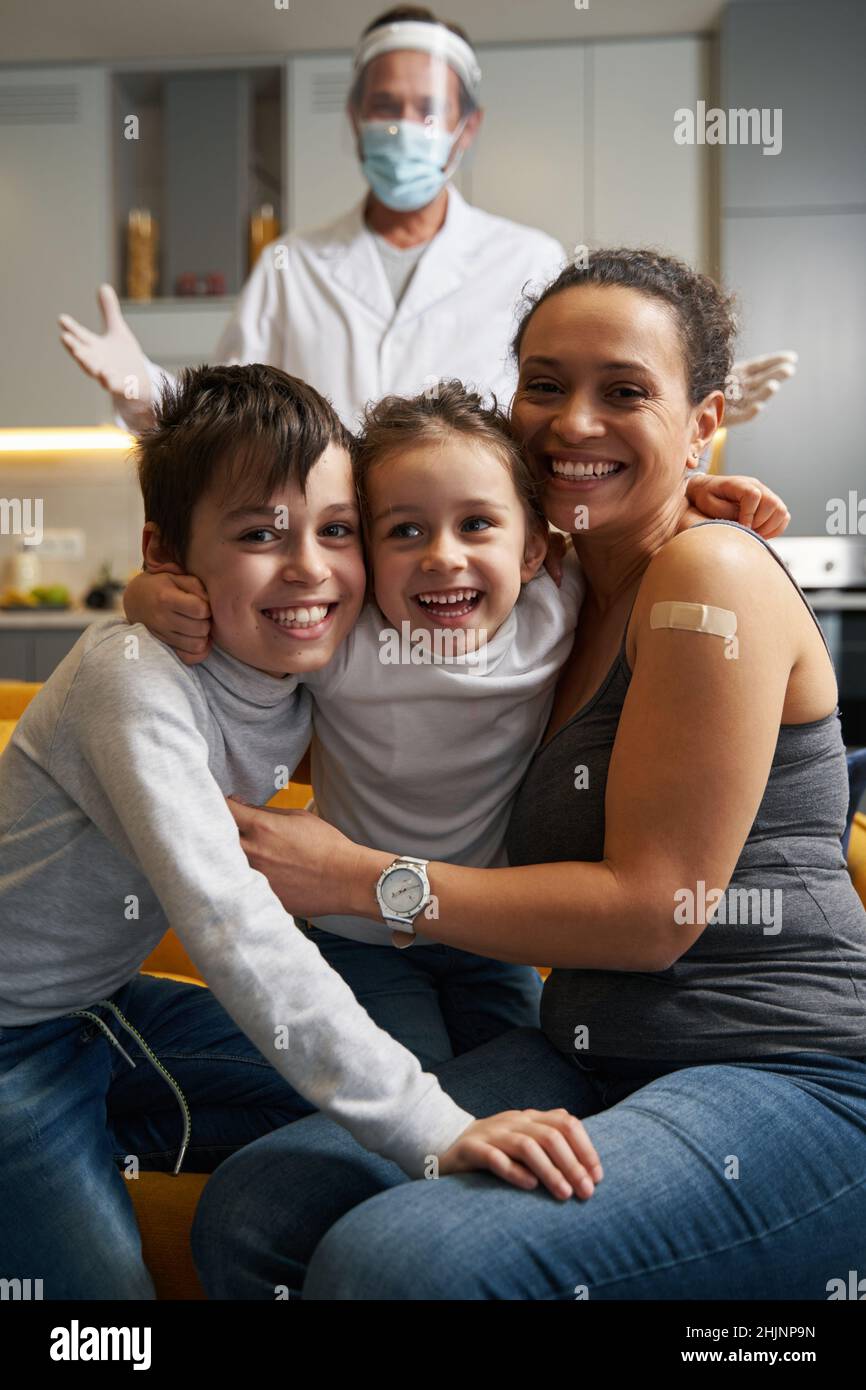 Famiglia felice sorridendo alla macchina fotografica con il medico dietro di loro Foto Stock