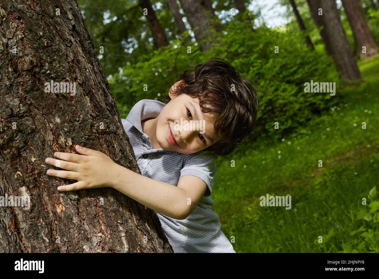 Ragazzo sorridente che abbraccia un albero in una foresta. . Primo piano ritratto di adolescente spensierato. Foto Stock