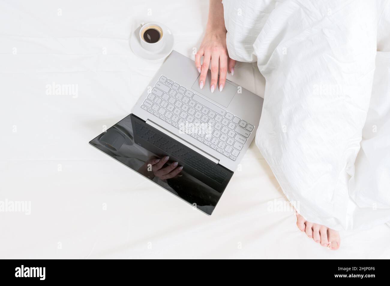 Il computer portatile si trova su un letto bianco accanto a una tazza di  caffè e una ragazza. Buongiorno. Lavoro da casa Foto stock - Alamy