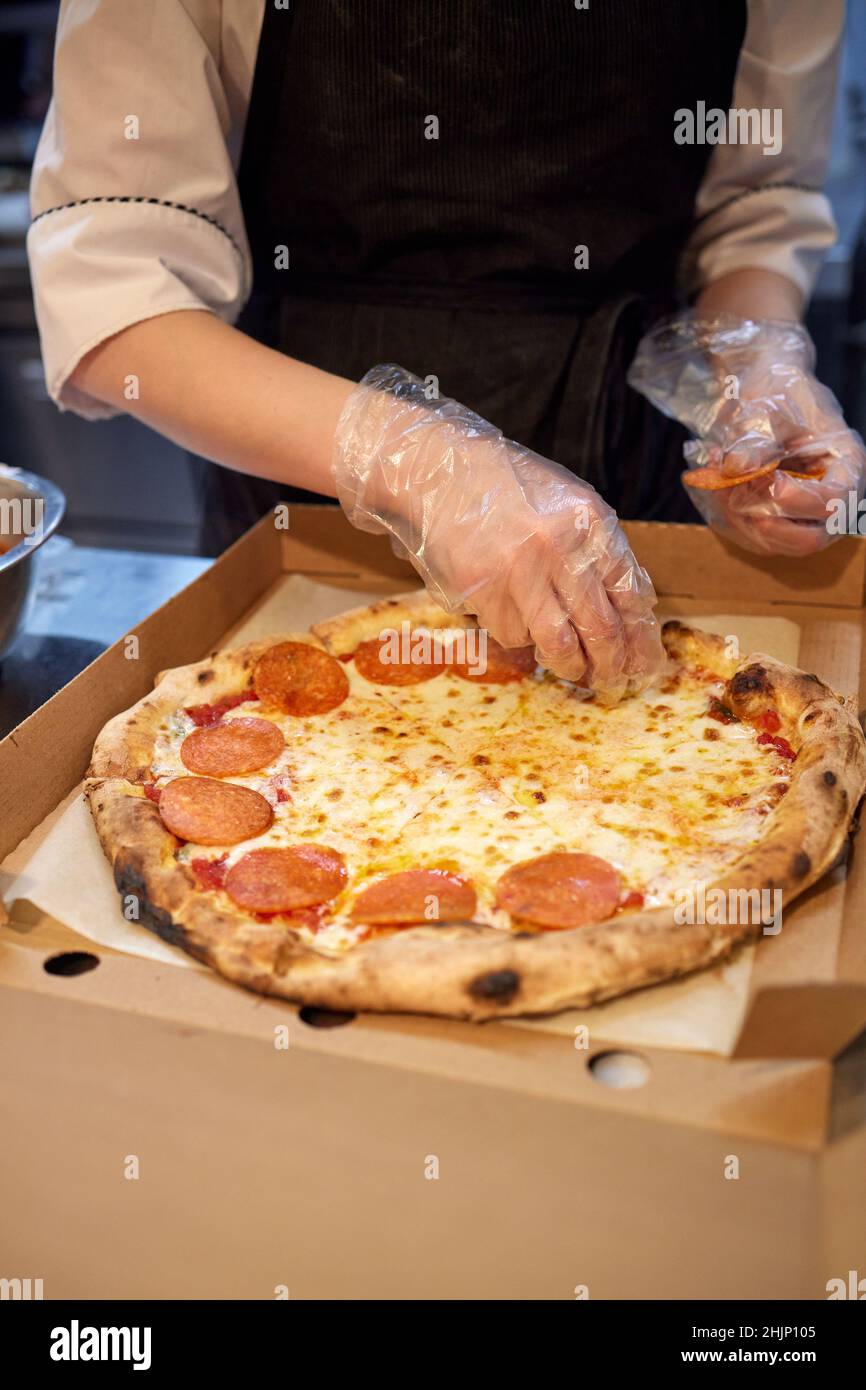 La macchina per la pizza mette gli ingredienti sull'impasto. Fare la pizza con salsiccia e salame Foto Stock