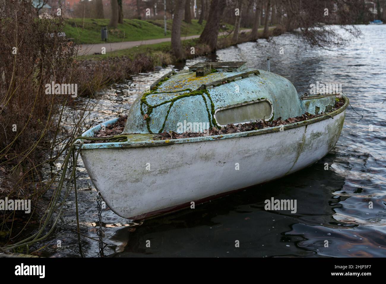 Piccola barca abbandonata in cabina in plastica rinforzata con fibra di vetro, cresciuta di muschio e lichene sulla riva di un lago in attesa di momenti migliori con Foto Stock