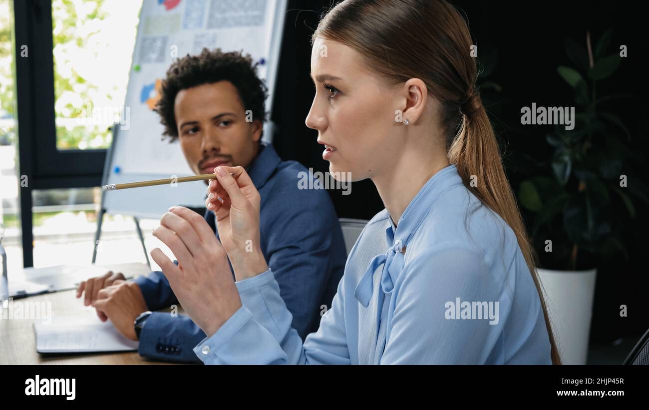 giovane donna d'affari che punta con la matita mentre siede vicino al collega afro-americano Foto Stock