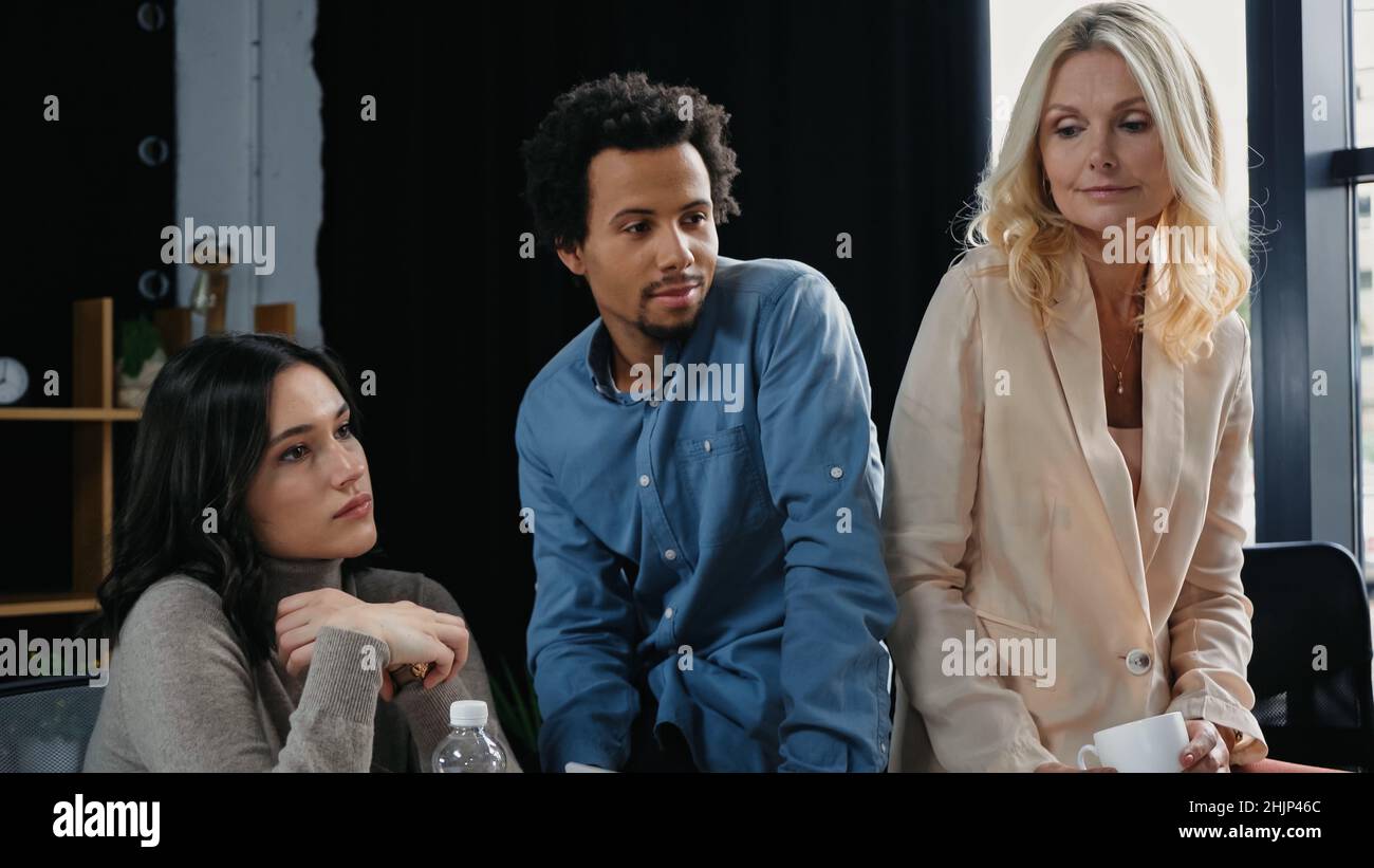 direttore afroamericano seduto vicino a donne d'affari ponderate in ufficio Foto Stock