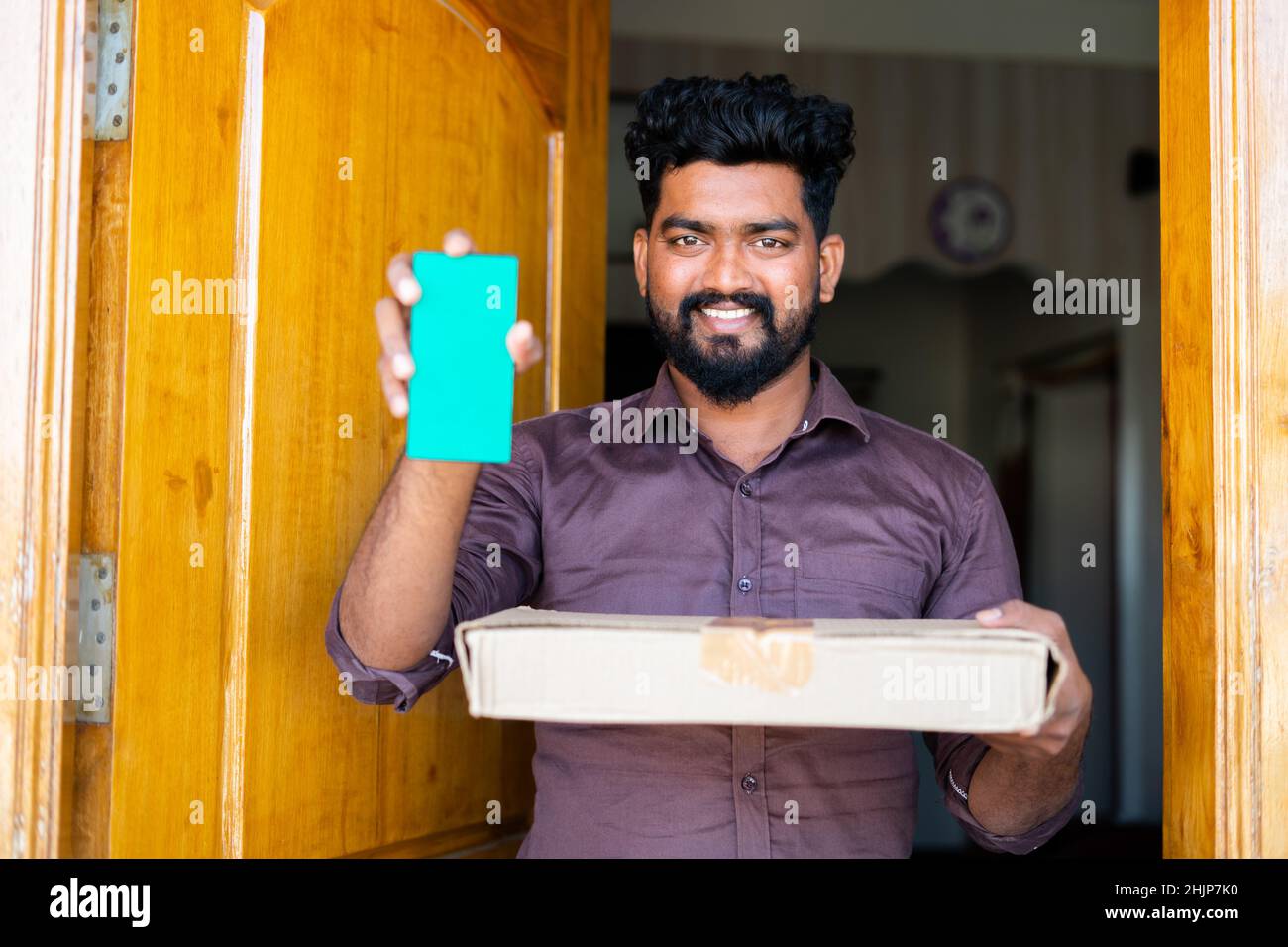 Cliente felice sorridente con il corriere in mano che mostra il telefono cellulare con schermo verde guardando la macchina fotografica a casa - concetto di servizio clienti felice e. Foto Stock