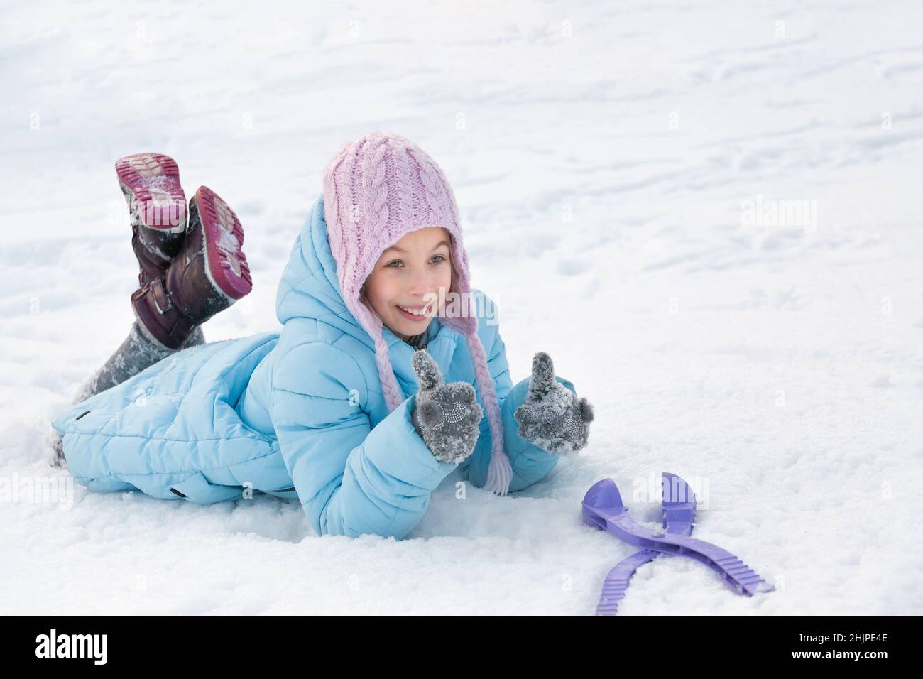 Ritratto di una ragazza in inverno in un cappello rosa e giacca blu. Ragazza si trova sulla neve. Ragazza che gioca nella neve Foto Stock