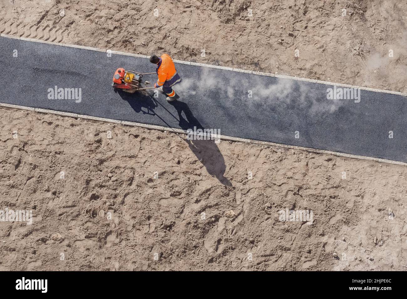 Asfalto caldo pavimentazione stradale costruzione cantiere uomo compattatore a piastre vibranti Rammer. Nuovo operatore di costruzione stradale che stesa la superficie di asfalto sulla passerella Foto Stock
