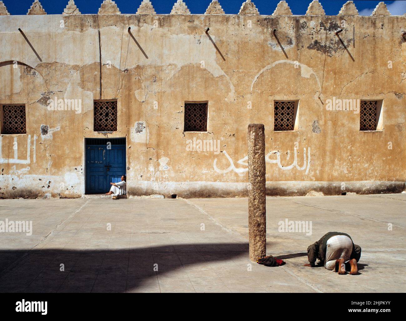 Un uomo sta pregando mentre il turista sta sta prendendo il sole nella moschea della città di Ta'izz, Yemen. Foto Stock