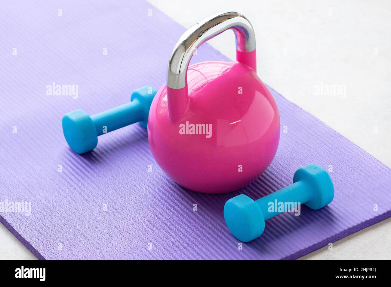 Primo piano di un peso luce blu su una stuoia viola yoga pilates sul pavimento di una palestra con un bollitore rosa Foto Stock