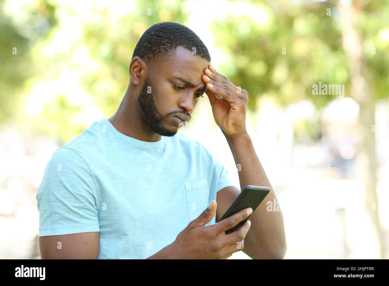 Uomo interessato con pelle nera che controlla le notizie dello smart phone in un parco Foto Stock