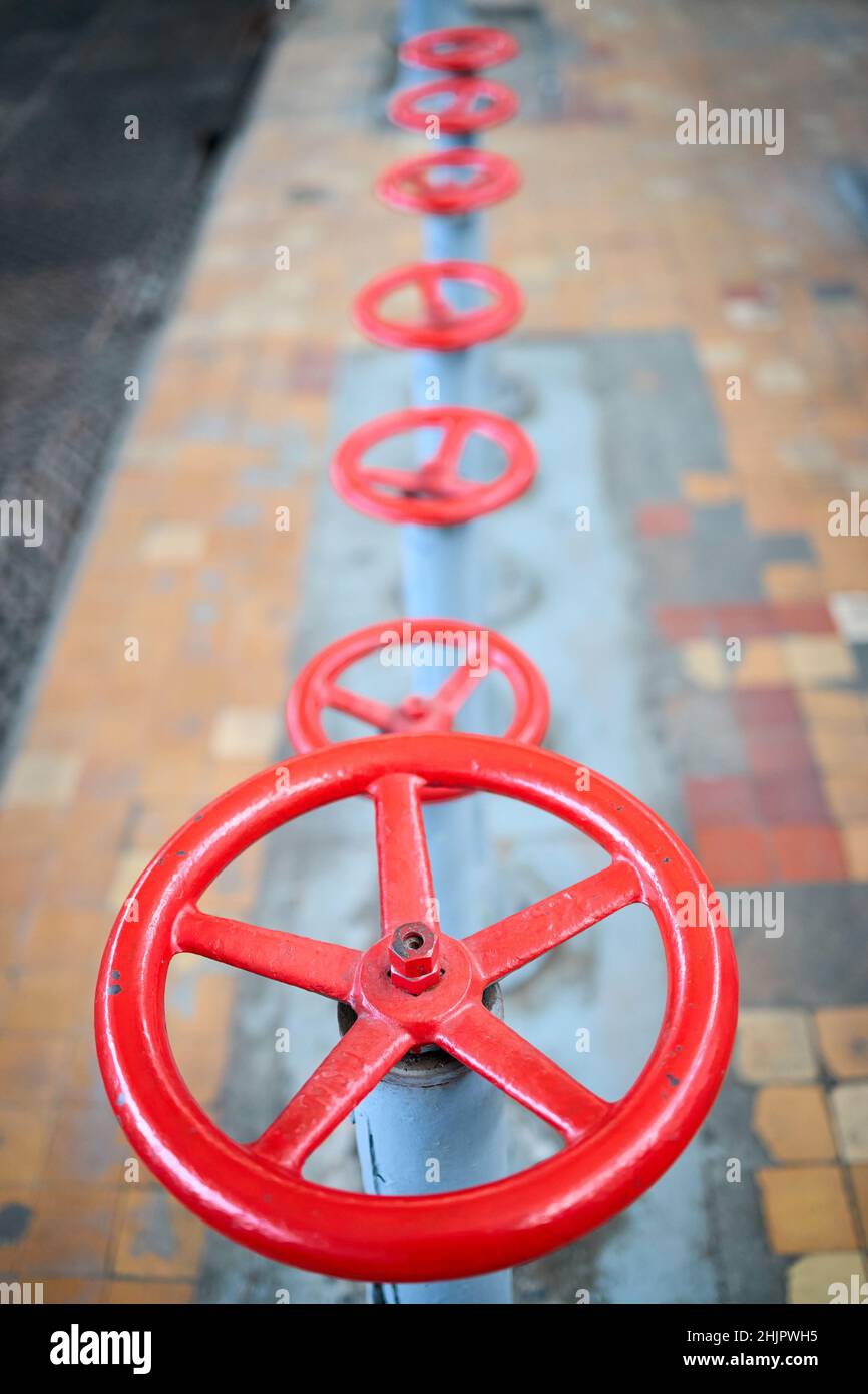 Fila di vecchie ruote retro-valvole verniciate rosso fuoco selettivo con dispositivo di estensione su sfondo fuori fuoco pavimento piastrellato e lamiera perforata Foto Stock