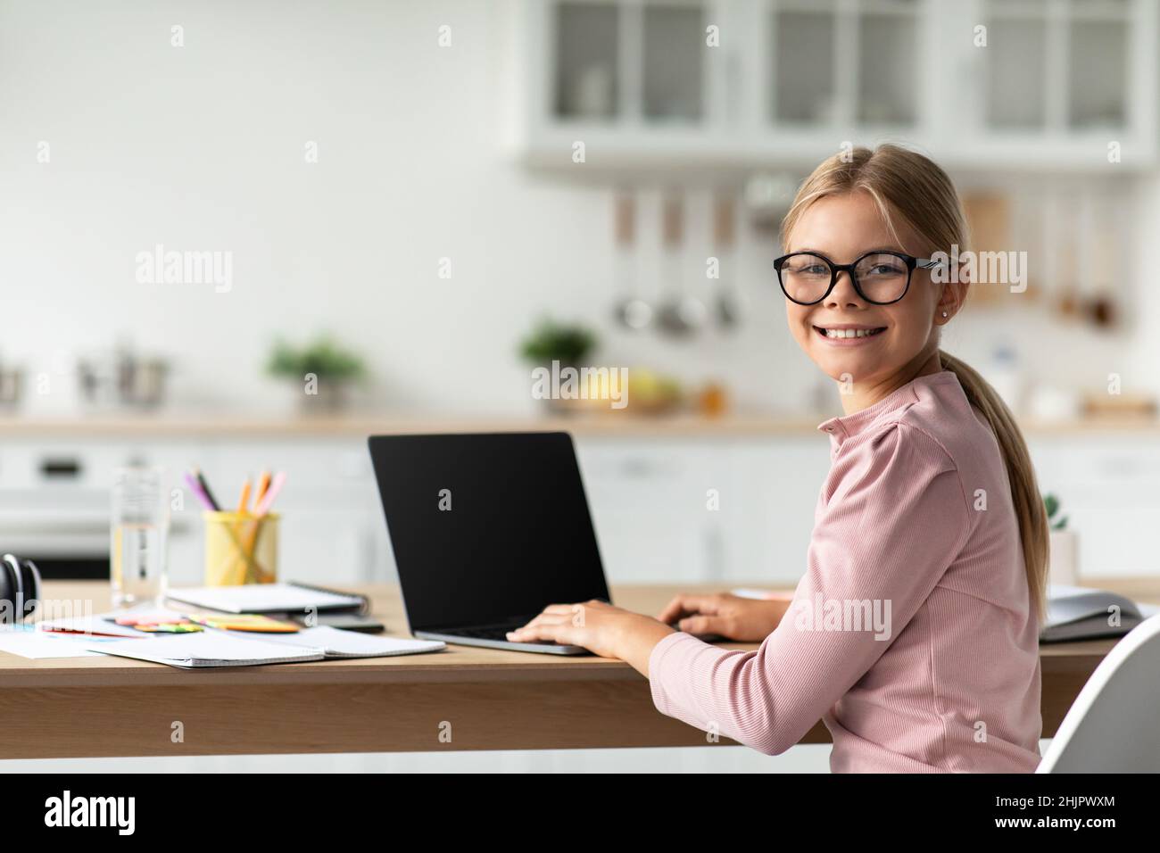 Allegra scolaretta caucasica in occhiali guardare la macchina fotografica al tavolo con il computer con schermo vuoto Foto Stock