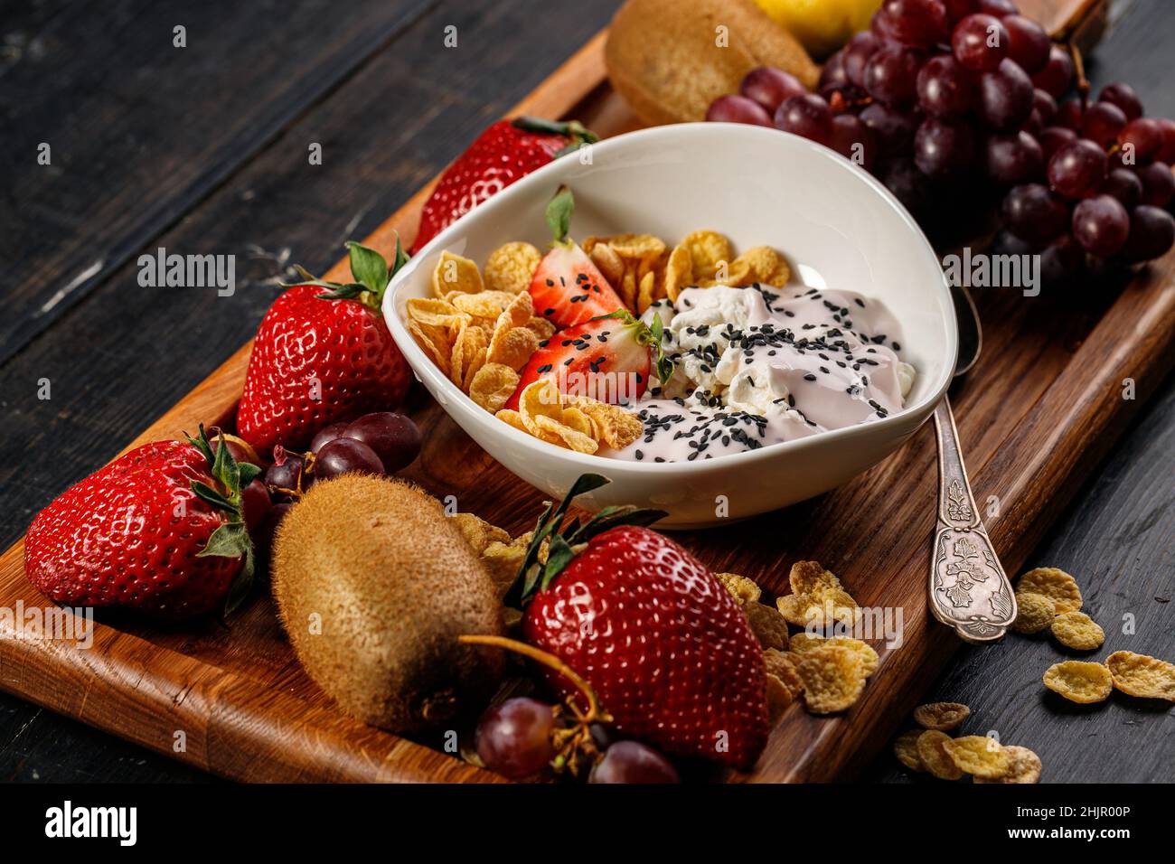 Fiocchi di mais con yogurt e semi di chia. Frutta fresca e succosa assortita. Fragola, kiwi, mela, pera, banana, uva. Deliziosa frutta tropicale su un bosco Foto Stock