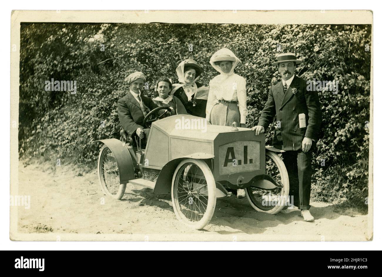 Cartolina originale dell'epoca edoardiana di turisti felici, uomini e donne che indossano barche in paglia e cappelli, vestiti con eleganti abiti domenicali, postazioni per una foto in una modellina di auto, attrezzatura fotografica (alcuni personaggi), durante una vacanza estiva al mare. La modella ha stranamente le lettere A.I. fotografate da H. Batty, The Jetty Studio, Clacton-on-Sea, Essex, Regno Unito circa 1910, 1912. Foto Stock