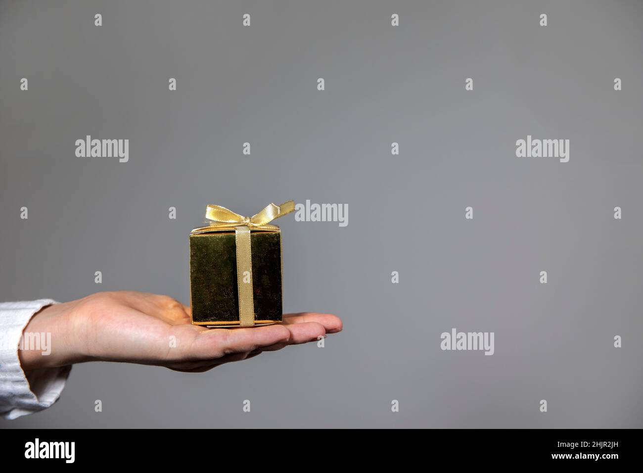 Mani che tengono la scatola del regalo d'oro isolato su sfondo grigio. Dare regalo, compleanno, Natale, giorno della madre altre feste con spazio copia Foto Stock