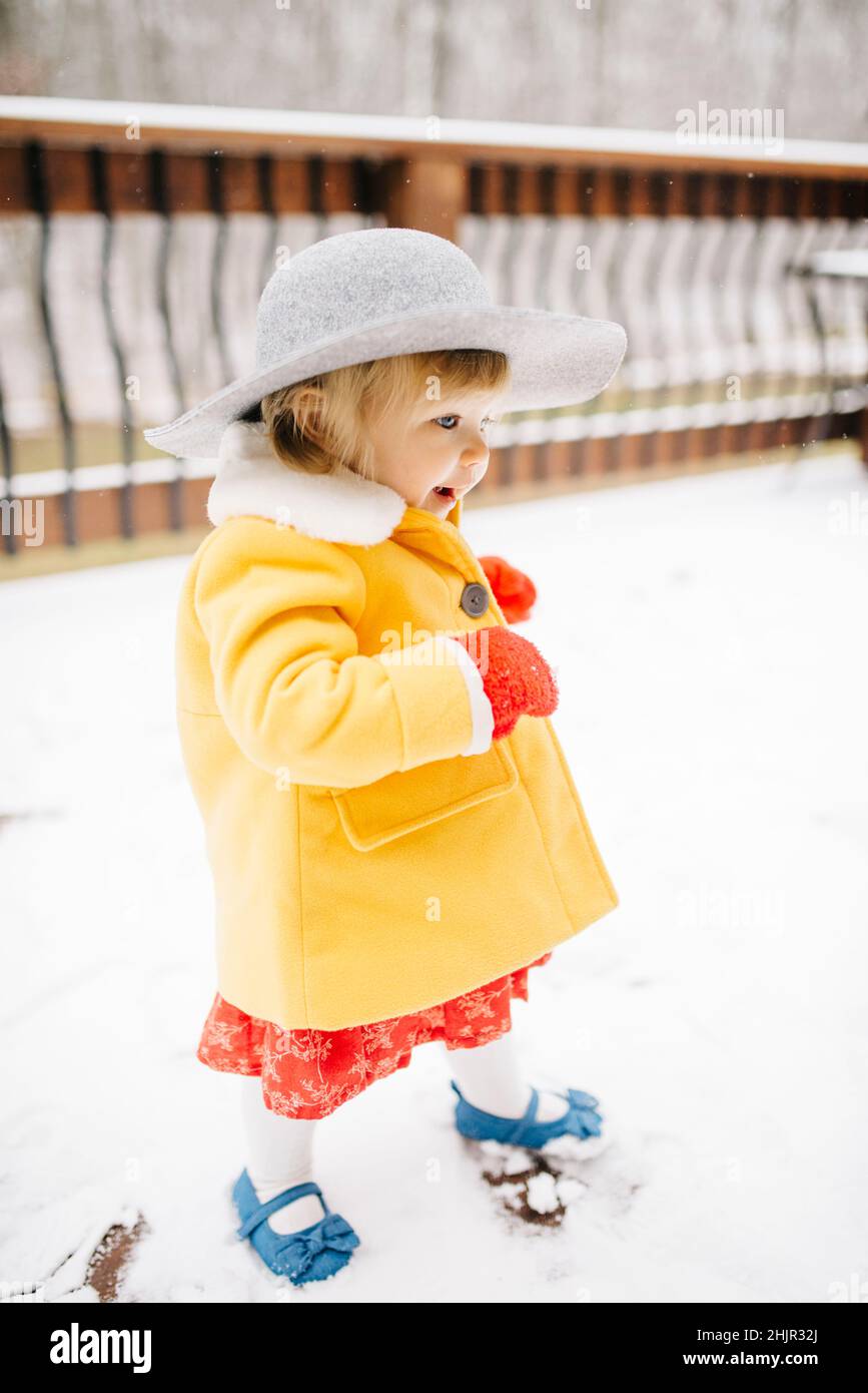 Bambina che cammina nella neve, indossa un cappello e un cappotto giallo Foto Stock
