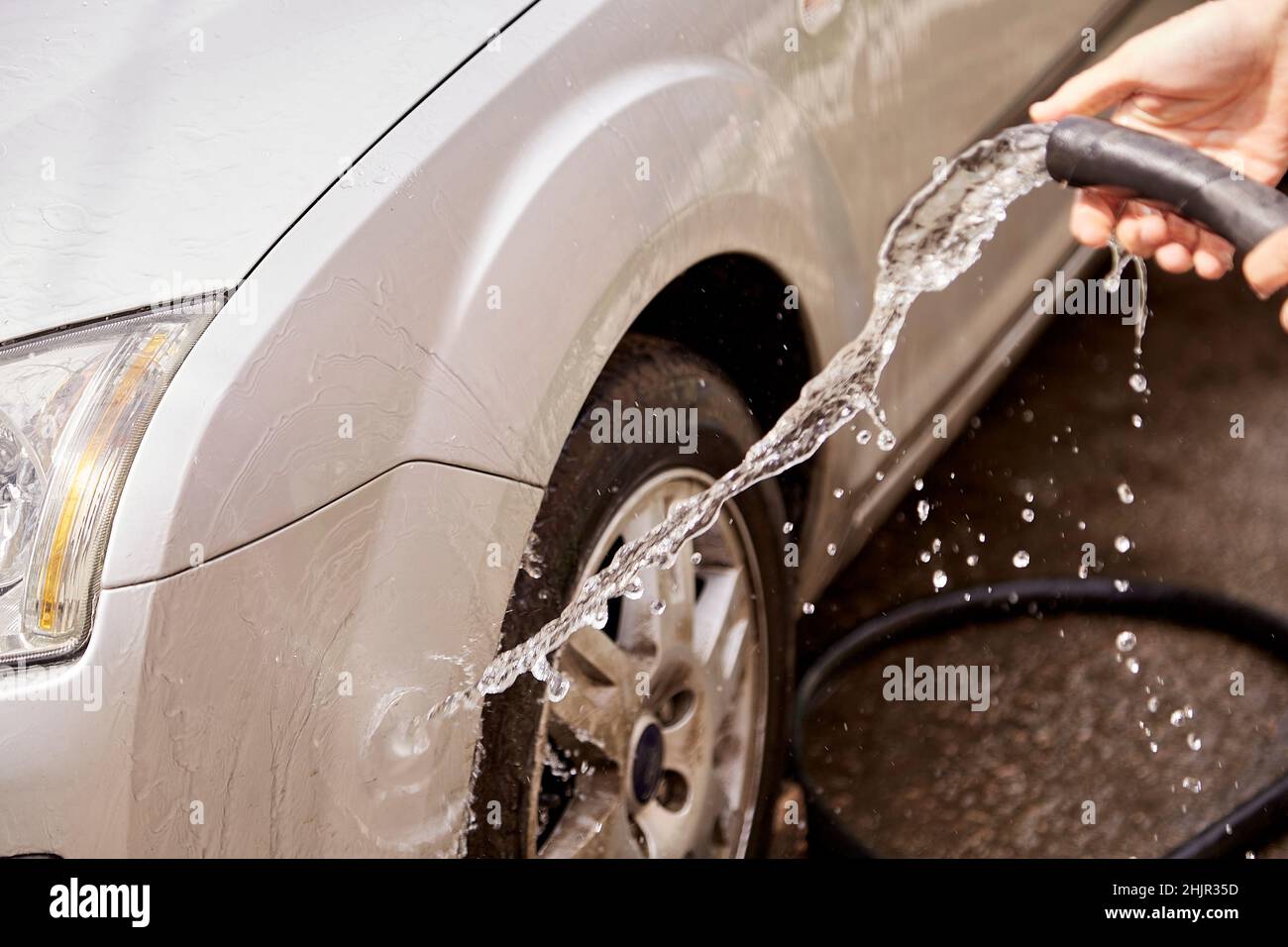 Lavare la vettura con acqua da sotto i tubi flessibili. Home routine. Manutenzione del veicolo. Foto Stock