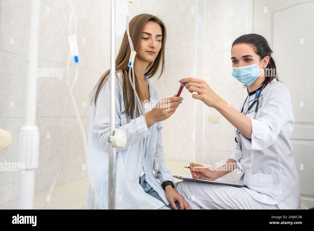 Paziente con provetta con sangue in posa in ospedale. Medico con appunti e paziente seduto sul divano Foto Stock
