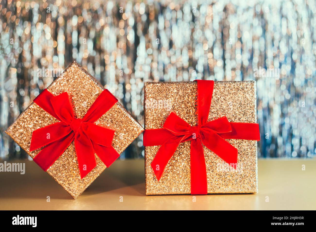 Luccicanti confezioni regalo dorate con nastro rosso velluto con un arco sullo scintillante sfondo in ninsel d'oro. Il concetto di un regalo per il compleanno, San Valentino' Foto Stock