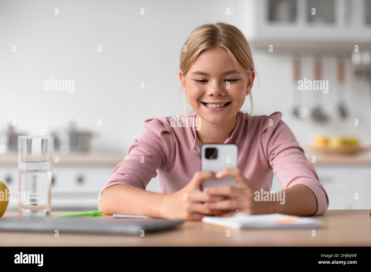 Allegro studente caucasico ragazza che chiacchiera al telefono, si siede al tavolo in cucina interna Foto Stock
