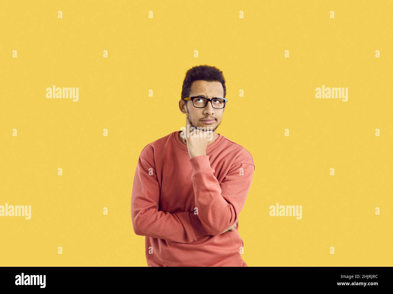 Puzzled studente maschile in occhiali isolati su sfondo giallo pensando a qualcosa Foto Stock