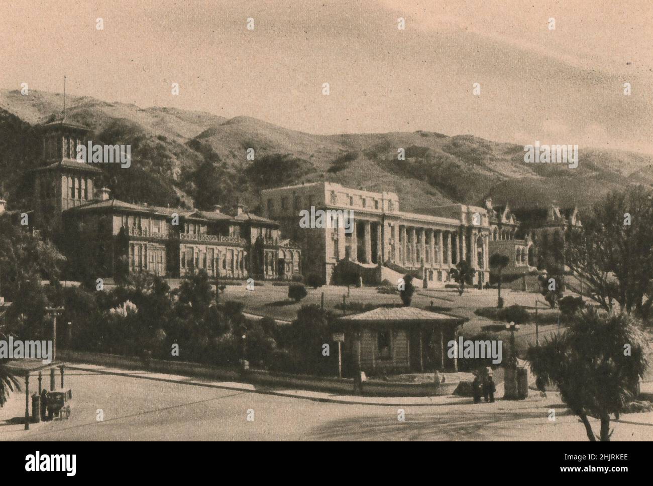 In piedi su una terrazza le Case del Parlamento e la loro bianca colonnade sono prominenti sullo sfondo di colline a Wellington. Nuova Zelanda (1923) Foto Stock
