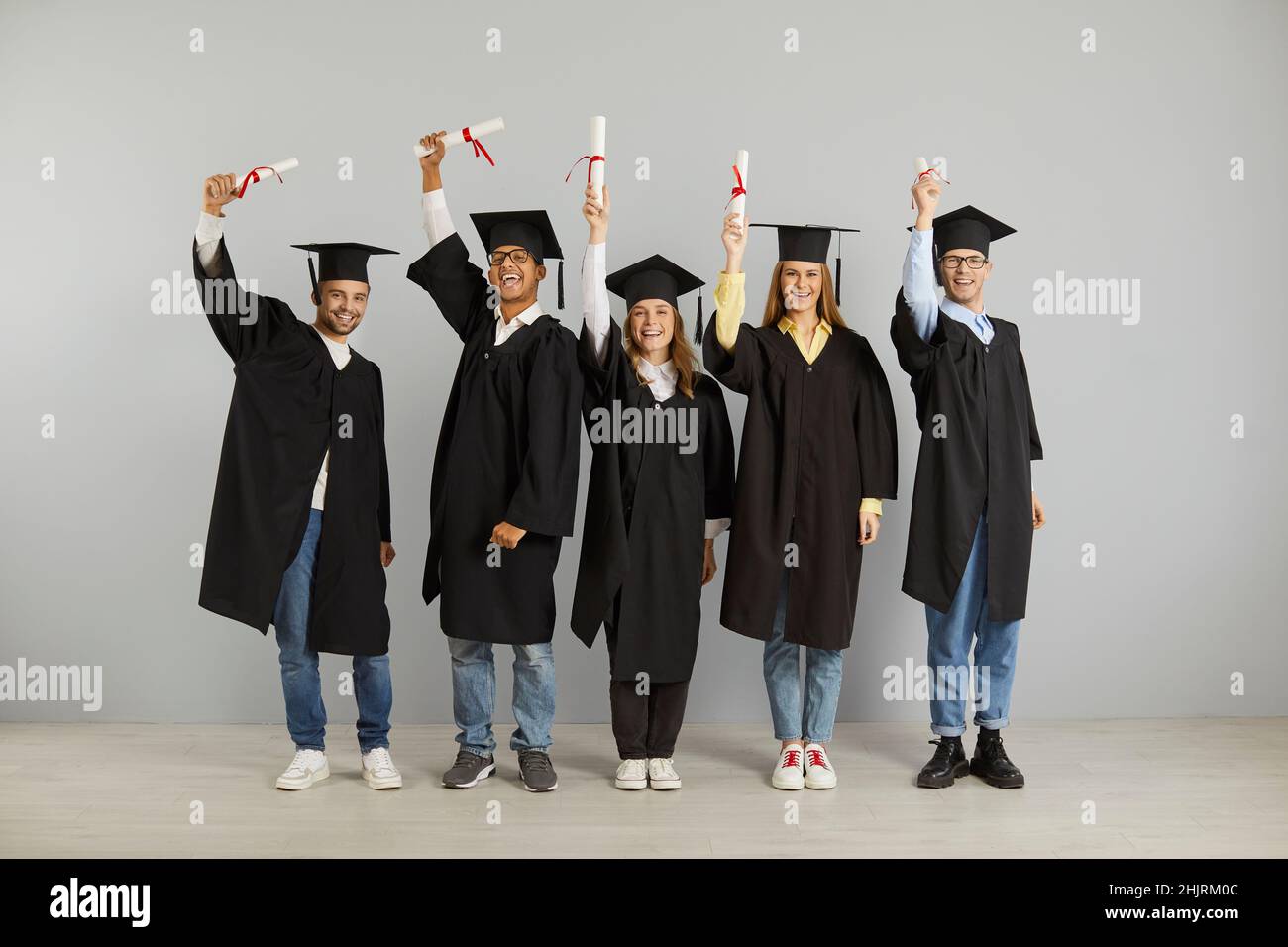 Gruppo di fortunati laureati multirazziali che tengono alto il loro diploma nelle loro mani. Foto Stock
