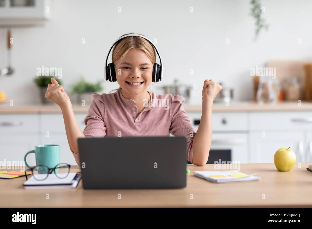 Felice allievo caucasico teen girl in cuffie si rallegra per successo di studio con il laptop a tavola Foto Stock