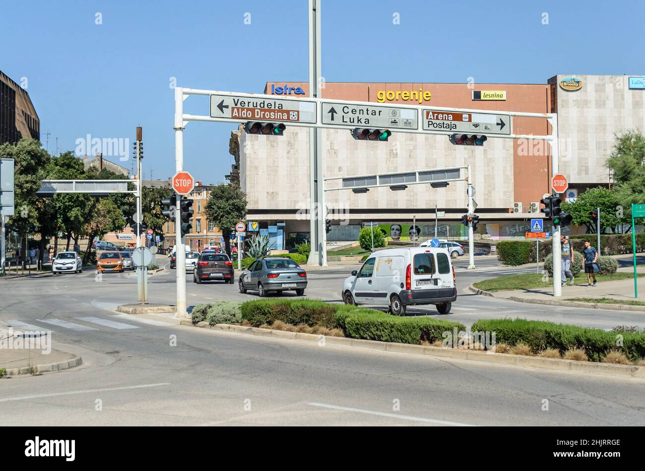 Strade nel centro di Pula. Veicoli in movimento, semafori e segnaletica direzionale in un giorno di sole. Giorno ordinario nella vita quotidiana. Foto Stock