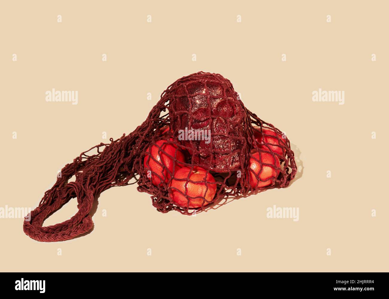 Tangerini e gabbiano umano glittered in un sacchetto marrone della stringa (eco-sacchetto della maglia, sacchetto del panno lavorato a maglia) su uno sfondo beige. Negozi moderni e riutilizzabili, senza rifiuti Foto Stock