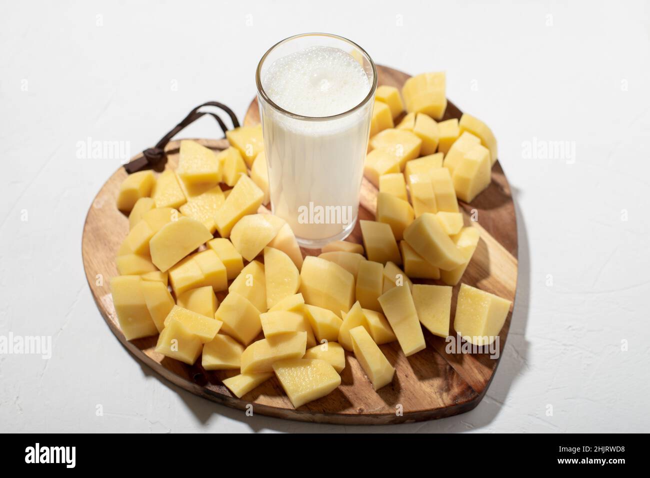 Concetto di latte di patate. Latte alternativo. Un bicchiere di latte su un asse di legno con patate crude tritate. Foto Stock