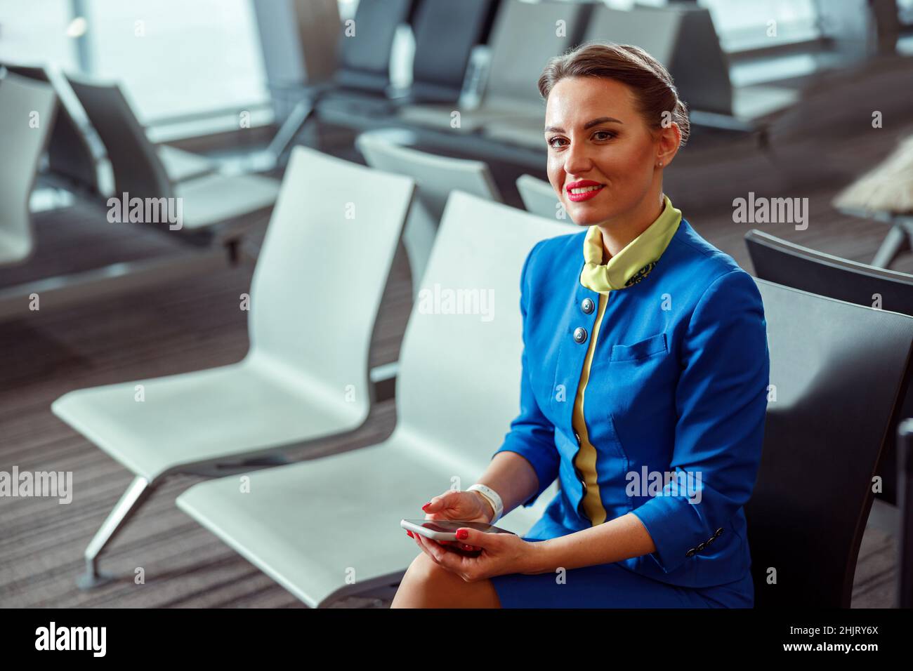 Donna gioiosa, stewardess seduto su sedia nella sala partenze aeroporto Foto Stock