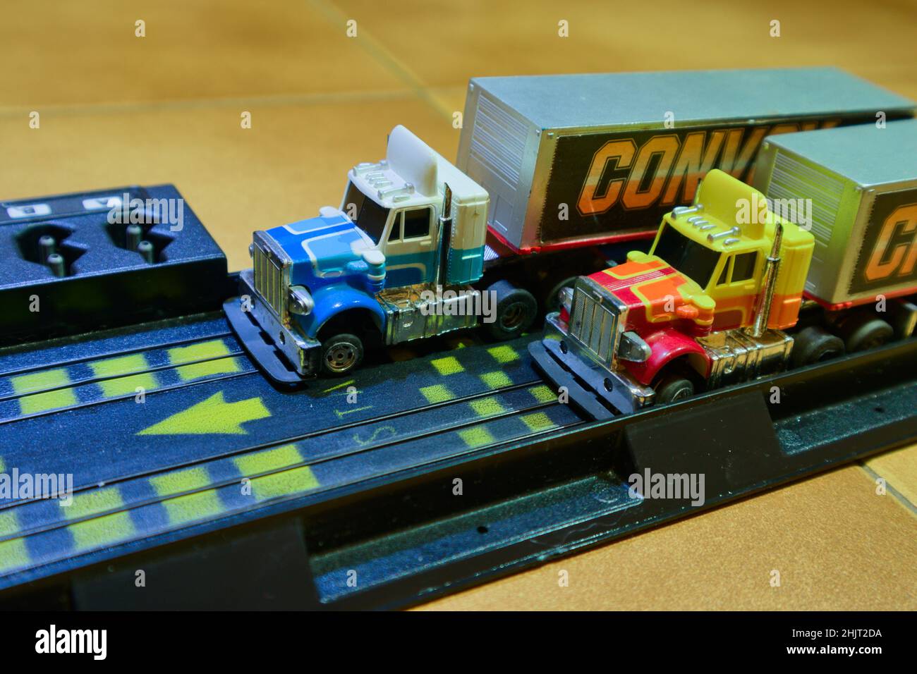 Immagine di piccoli camion con cabine multicolore all'uscita di un circuito giocattolo installato sul pavimento della stanza dei bambini Foto Stock