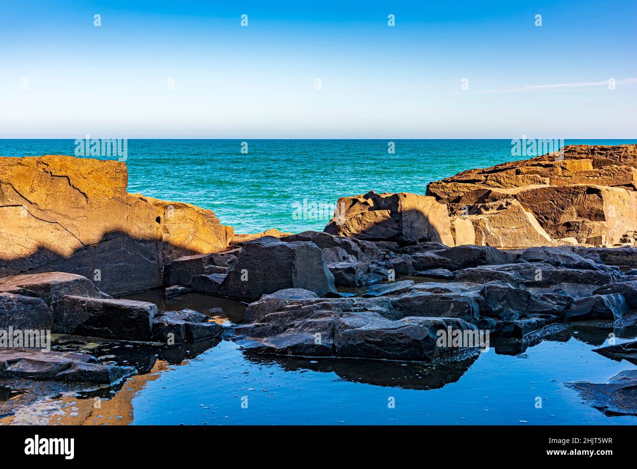 Formazione rocciosa di fronte al mare e l'orizzonte in un pomeriggio di cielo blu nella città di Torres, Rio Grande do sul, Brasile Foto Stock