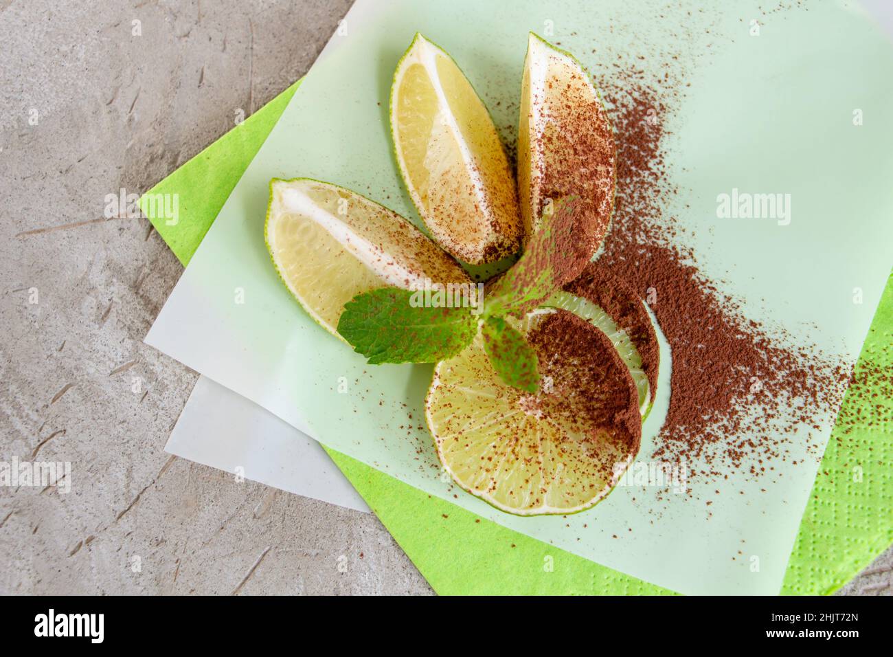 spicchi di lime e un rametto di menta, cosparsi di cacao su sfondo concreto Foto Stock