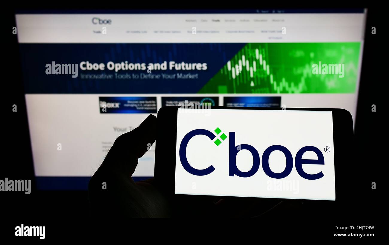 Persona che tiene uno smartphone con il logo della società finanziaria statunitense CBOE Global Markets Inc. Sullo schermo di fronte al sito Web. Mettere a fuoco sul display del telefono. Foto Stock