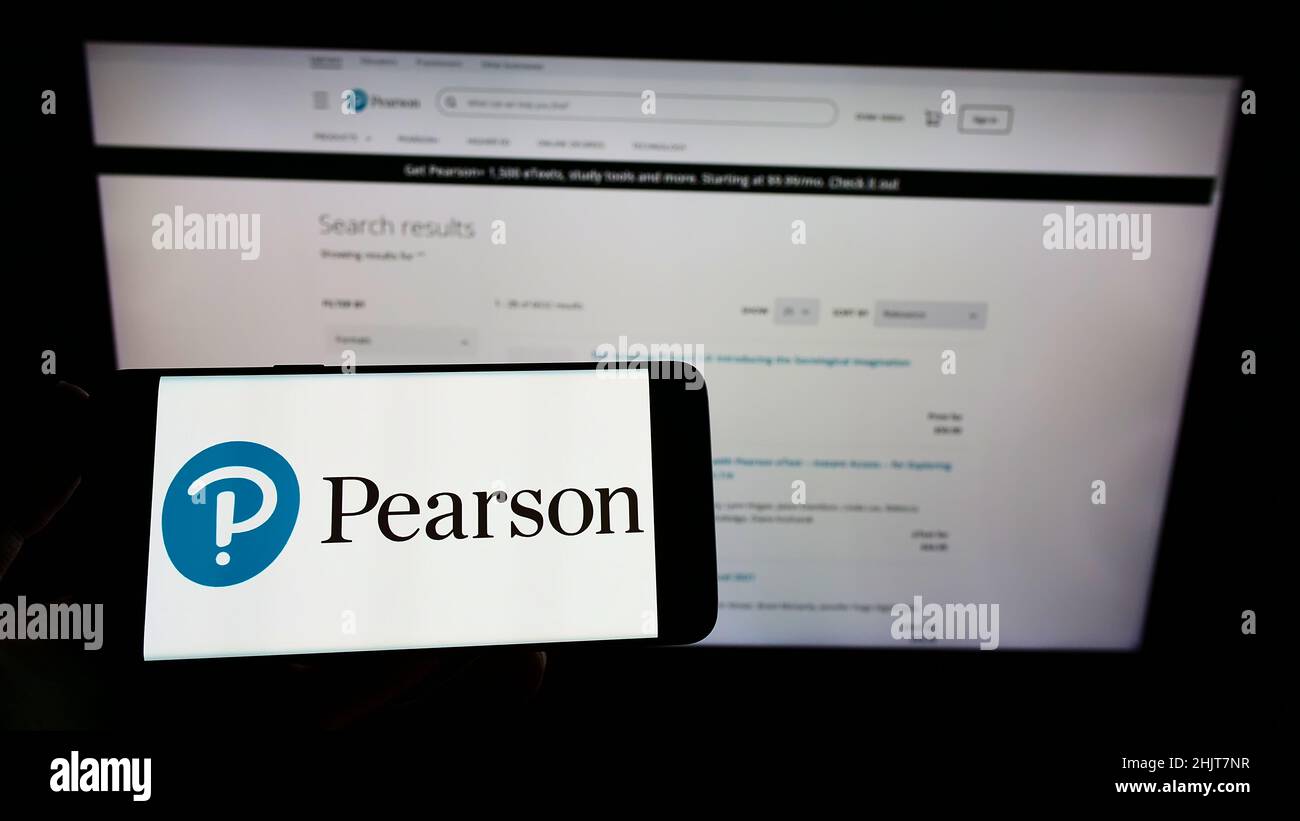 Persona che tiene uno smartphone con il logo della società di pubblicazione britannica Pearson plc sullo schermo di fronte al sito Web. Mettere a fuoco sul display del telefono. Foto Stock