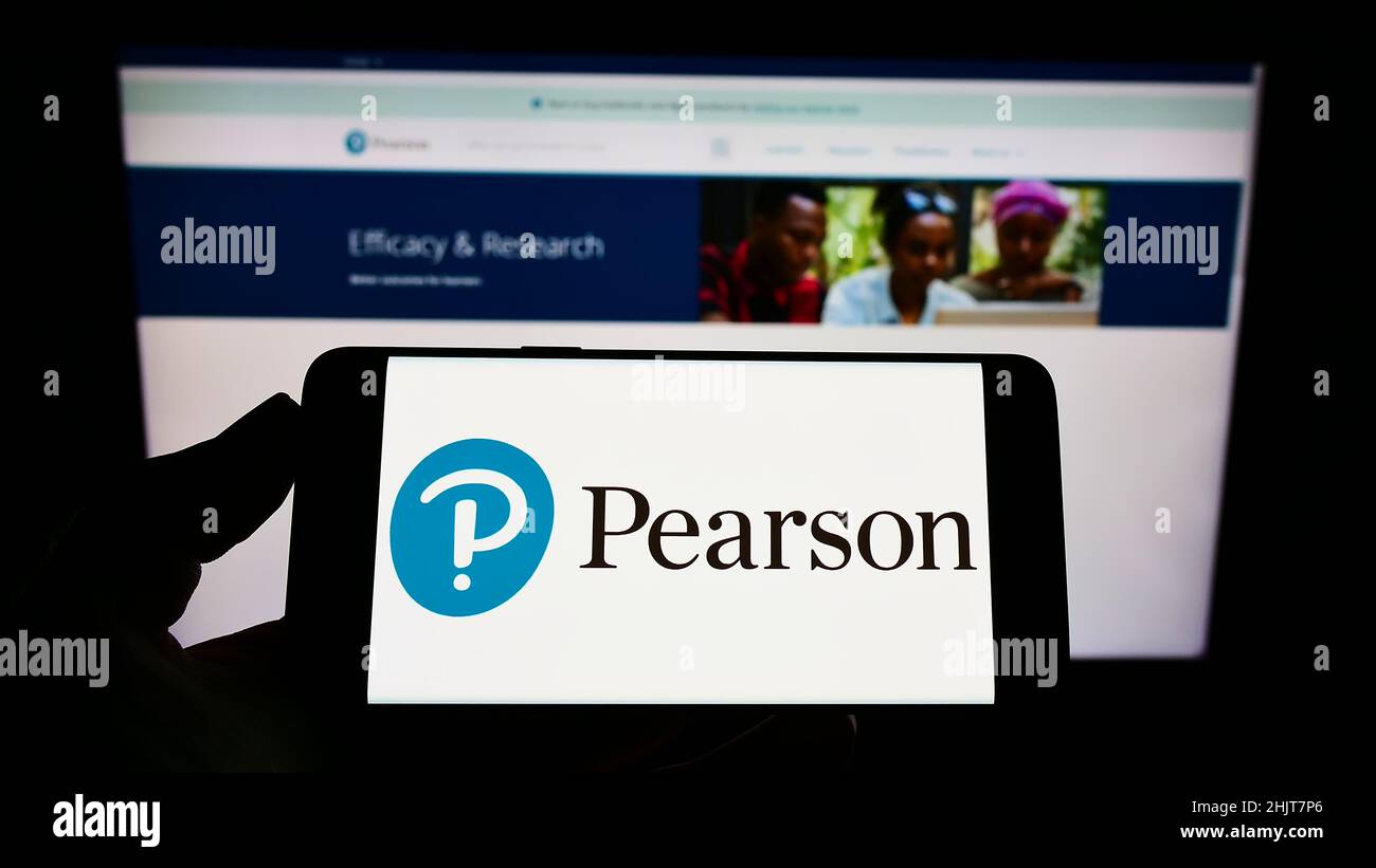 Persona che detiene il telefono cellulare con il logo della società di pubblicazione britannica Pearson plc sullo schermo di fronte alla pagina Web aziendale. Mettere a fuoco sul display del telefono. Foto Stock
