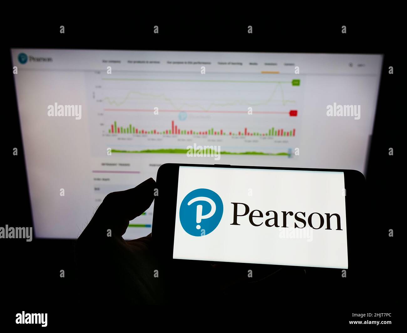 Persona che tiene il cellulare con il logo della società di pubblicazione britannica Pearson plc sullo schermo di fronte al sito web aziendale. Mettere a fuoco sul display del telefono. Foto Stock