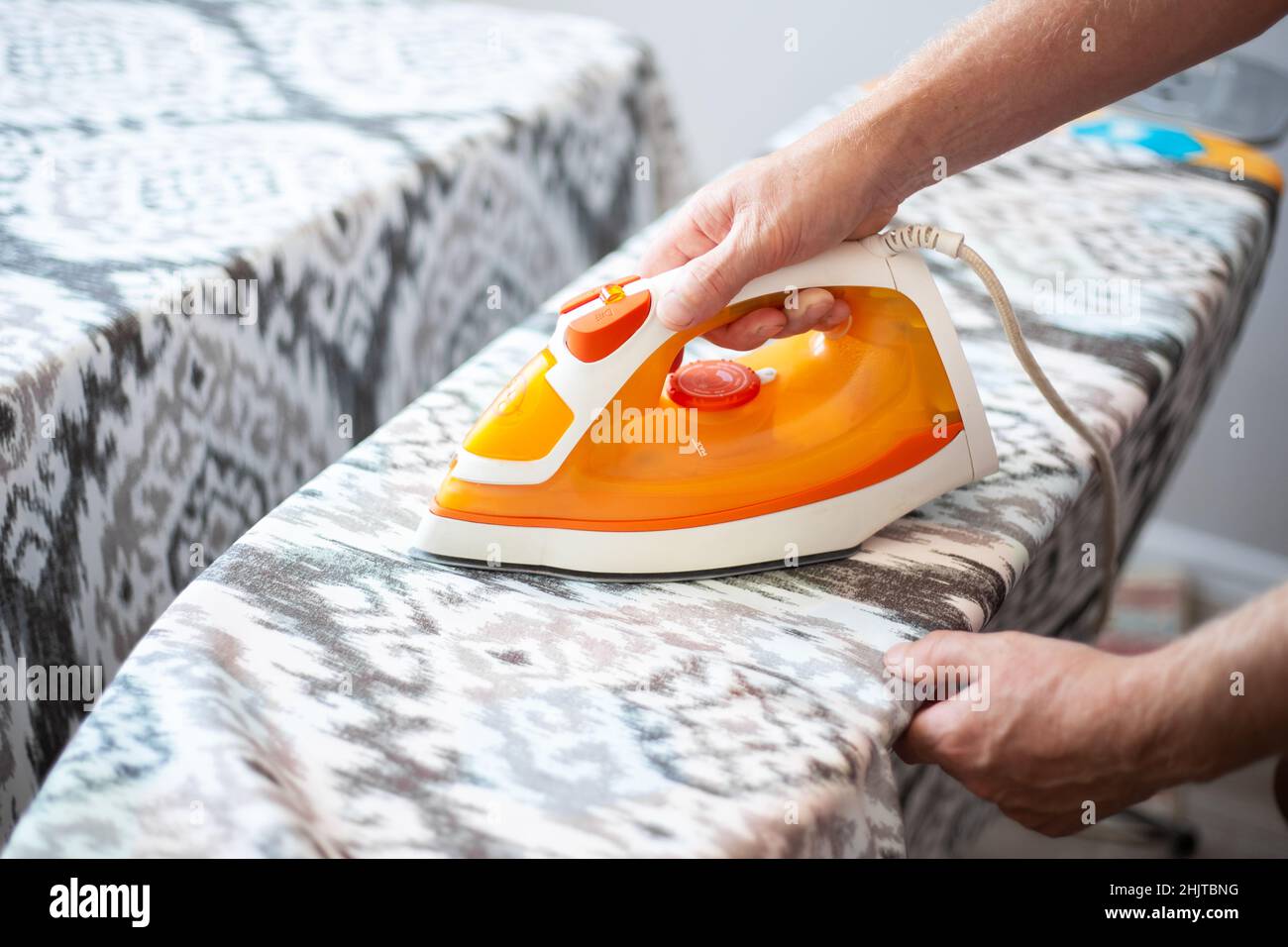 Un uomo tiene in mano un ferro da stiro, stirando le tende su un asse da stiro. Le faccende domestiche. Foto Stock