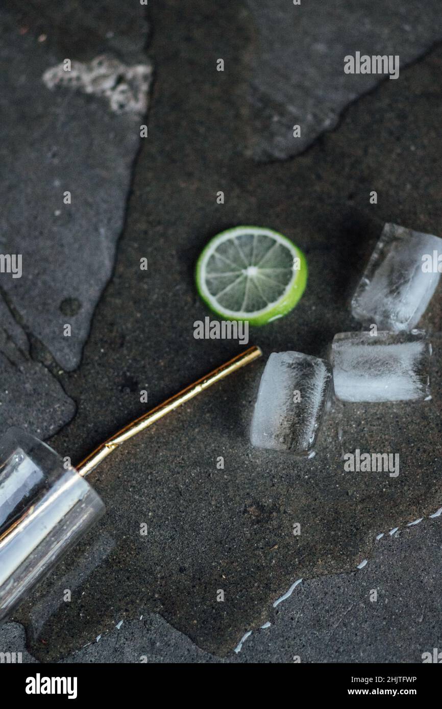 non piangere sopra la bevanda versata: bussa sopra il vetro con liquido chiaro, lime, ghiaccio rettangolare, paglia potabile della carta d'oro su pavimento di calcestruzzo Foto Stock