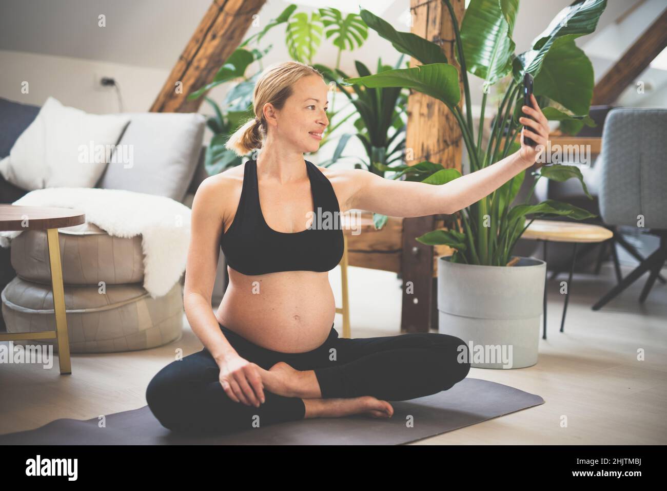 Giovane felice e allegra bella donna incinta prendendo selfie con il suo cellulare, pur rimanendo in forma, sportiva e attiva sul suo congedo di maternità Foto Stock