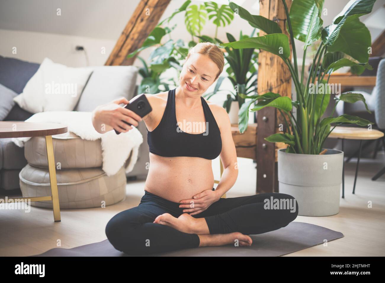 Giovane felice e allegra bella donna incinta prendendo selfie con il suo cellulare, pur rimanendo in forma, sportiva e attiva sul suo congedo di maternità Foto Stock