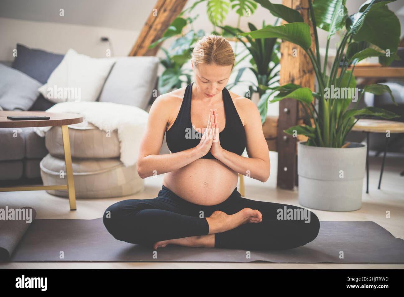 Giovane bella donna incinta che pratica yoga a casa nel suo soggiorno. Maternità, gravidanza, stile di vita sano e concetto di yoga Foto Stock