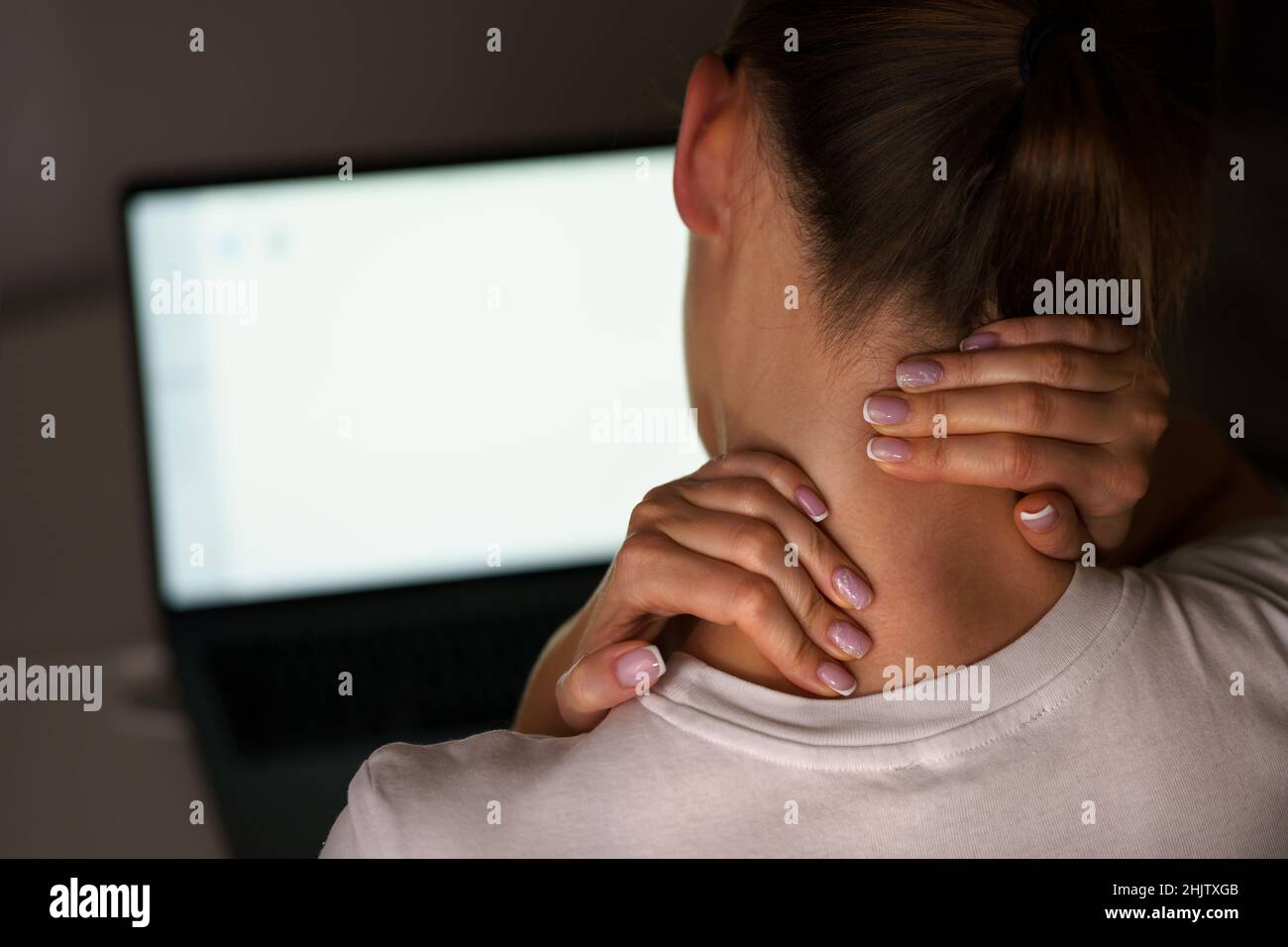 Giovane donna che soffre di dolore al collo dopo aver lavorato al computer. Massaggio del collo per alleviare il dolore Foto Stock