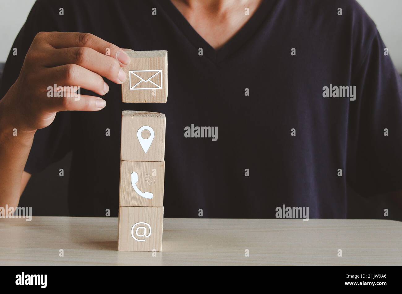 Mano che tiene cubo di legno blocco icona lettera telefono posizione e indirizzo su Table.Business comunicazione e sociale concetto di rete. Foto Stock